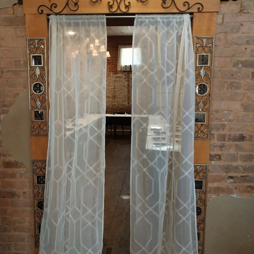 An ornate iron-topped doorway with sheer curtains leading into the brick dining room