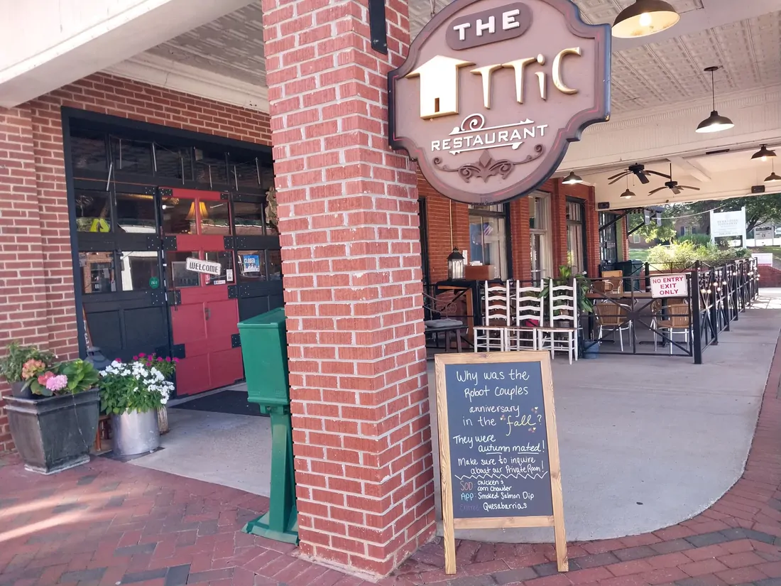 The Attic Restaurant storefront in downtown Clarkesville with its hanging sign, brick column, and the original red garage door
